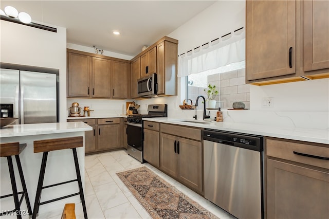 kitchen with a kitchen bar, sink, stainless steel appliances, and light stone counters