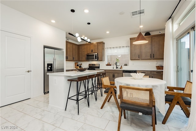 kitchen featuring hanging light fixtures, sink, a center island, stainless steel appliances, and a breakfast bar