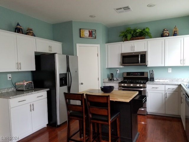 kitchen with light stone countertops, appliances with stainless steel finishes, dark hardwood / wood-style floors, and white cabinetry