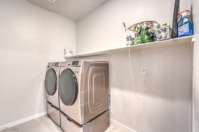 washroom with light tile patterned floors, laundry area, washing machine and dryer, and baseboards