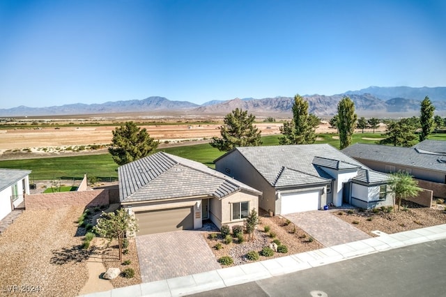 ranch-style home with decorative driveway, a mountain view, an attached garage, and stucco siding