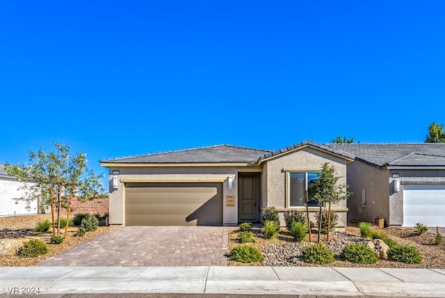 ranch-style home featuring decorative driveway, an attached garage, a tile roof, and stucco siding