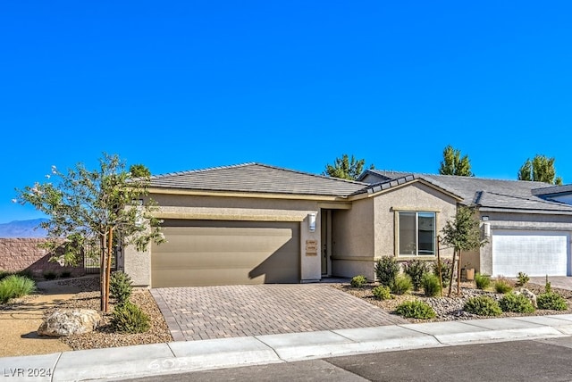 view of front of home featuring decorative driveway, an attached garage, a tile roof, and stucco siding