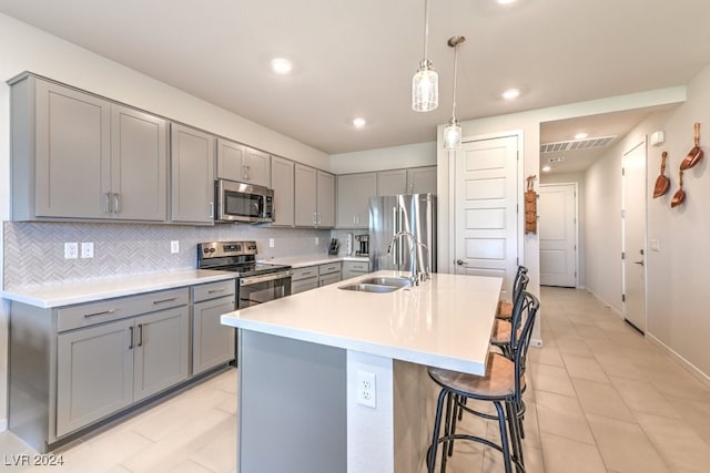 kitchen with stainless steel appliances, gray cabinets, light countertops, a kitchen island with sink, and a sink