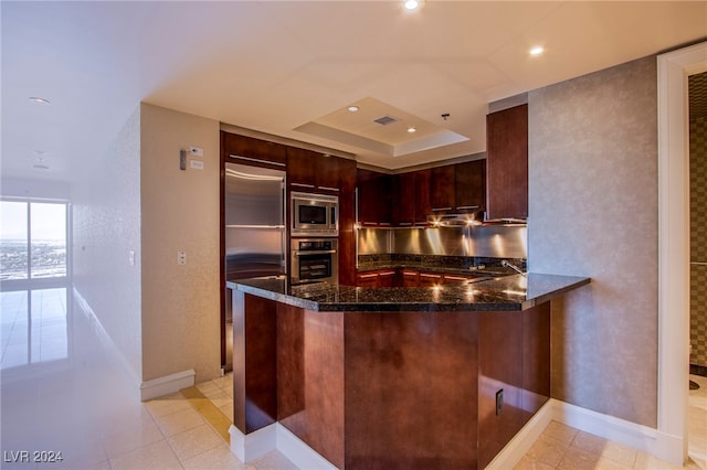 kitchen with dark stone counters, kitchen peninsula, light tile patterned flooring, and built in appliances