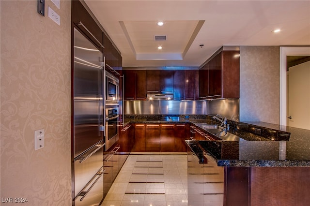 kitchen with dark stone countertops, sink, appliances with stainless steel finishes, and kitchen peninsula