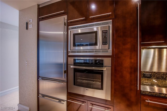 kitchen with dark stone counters, stainless steel appliances, dark brown cabinetry, and light tile patterned flooring