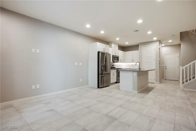 kitchen with appliances with stainless steel finishes, tasteful backsplash, light tile patterned floors, white cabinets, and an island with sink