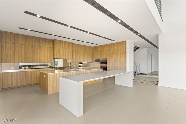 kitchen with a spacious island, light tile patterned flooring, and sink