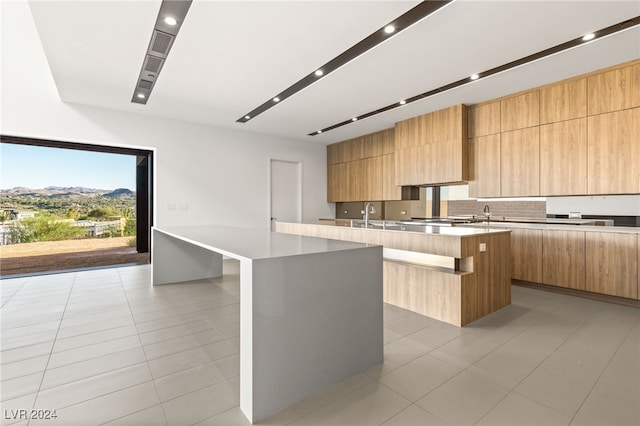 kitchen featuring decorative backsplash, light tile patterned flooring, a kitchen bar, and a kitchen island with sink