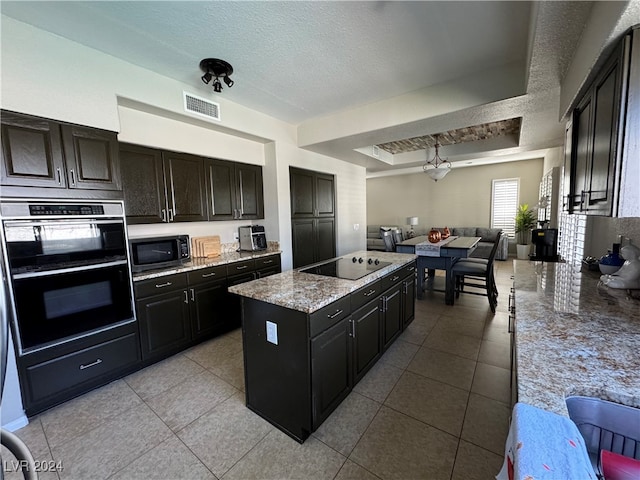 kitchen with light tile patterned floors, black appliances, a textured ceiling, and a kitchen island