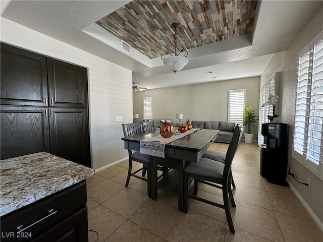 tiled dining room featuring a textured ceiling, ceiling fan, and a raised ceiling