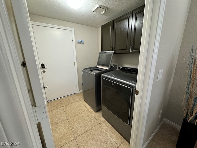 washroom with light tile patterned floors, a textured ceiling, washing machine and dryer, and cabinets