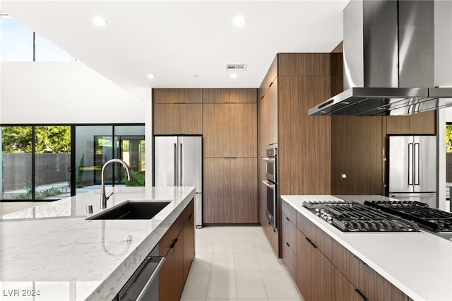 kitchen featuring wall chimney exhaust hood, sink, appliances with stainless steel finishes, and light stone counters