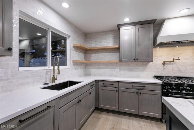 kitchen featuring light hardwood / wood-style flooring, custom range hood, sink, decorative backsplash, and high end stainless steel range oven