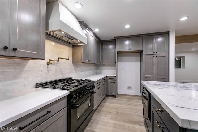 kitchen with light wood-type flooring, high end black range, backsplash, custom range hood, and light stone countertops