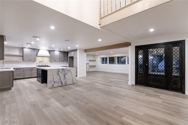 kitchen featuring light stone counters, custom exhaust hood, gray cabinets, a center island, and light wood-type flooring