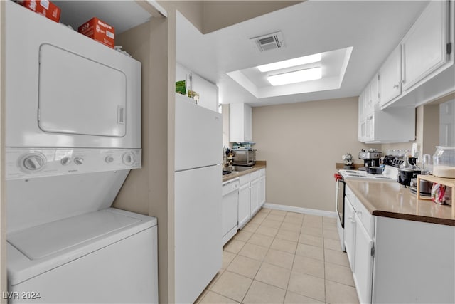 kitchen featuring stacked washer and dryer, white appliances, white cabinetry, and light tile patterned floors