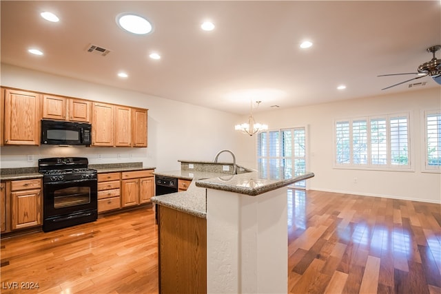 kitchen with light hardwood / wood-style floors, light stone counters, ceiling fan with notable chandelier, pendant lighting, and black appliances