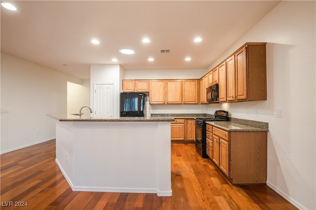 kitchen featuring black appliances, a center island with sink, and hardwood / wood-style floors