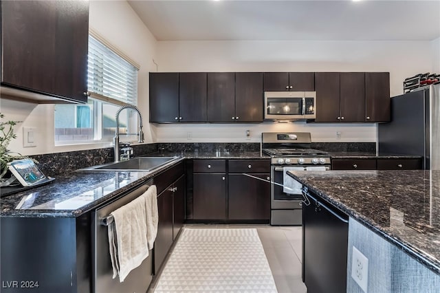 kitchen featuring dark stone counters, sink, dark brown cabinetry, light tile patterned floors, and appliances with stainless steel finishes