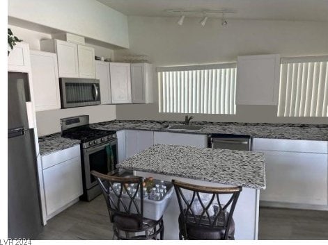 kitchen featuring light stone counters, sink, white cabinetry, stainless steel appliances, and a kitchen breakfast bar