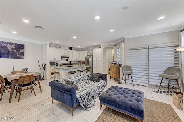 living room featuring light wood-type flooring, crown molding, and sink