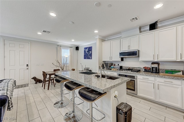 kitchen with white cabinets, an island with sink, sink, appliances with stainless steel finishes, and light stone countertops