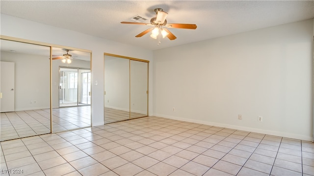 unfurnished bedroom with light tile patterned floors, a textured ceiling, multiple closets, and ceiling fan