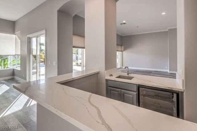 kitchen with light stone counters, wine cooler, sink, light hardwood / wood-style flooring, and crown molding