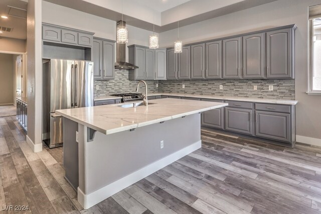 kitchen featuring stainless steel fridge, tasteful backsplash, light stone countertops, an island with sink, and hardwood / wood-style flooring