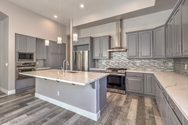 kitchen featuring pendant lighting, an island with sink, wall chimney range hood, appliances with stainless steel finishes, and dark hardwood / wood-style flooring