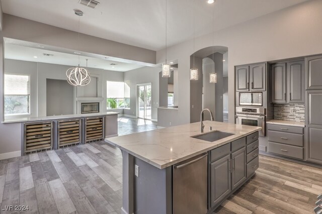 kitchen featuring a kitchen island with sink, wood-type flooring, sink, appliances with stainless steel finishes, and wine cooler