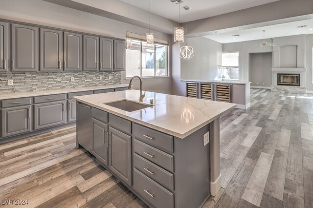 kitchen featuring a kitchen island with sink, gray cabinetry, pendant lighting, sink, and stainless steel dishwasher