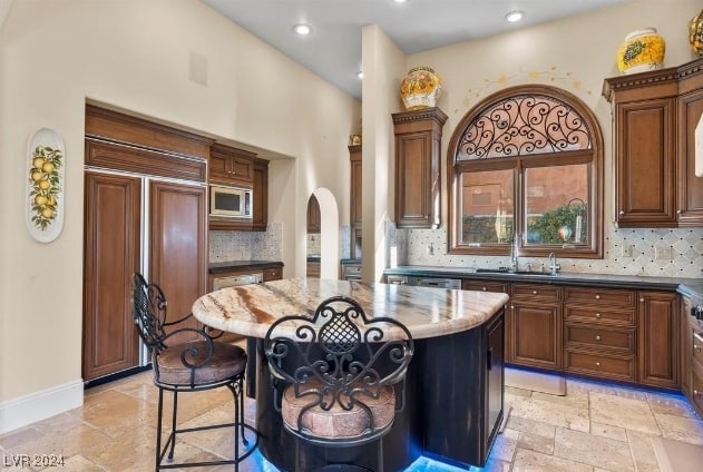 kitchen with dark stone countertops, backsplash, a center island, and built in appliances