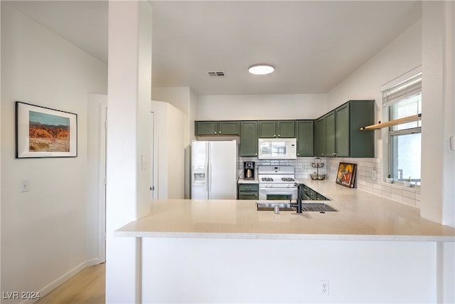 kitchen featuring light wood-type flooring, white appliances, green cabinets, sink, and kitchen peninsula