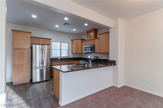 kitchen with kitchen peninsula, dark stone countertops, dark hardwood / wood-style floors, and stainless steel appliances