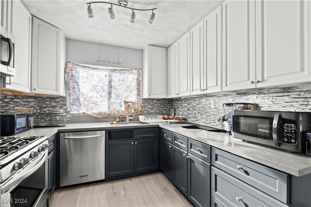 kitchen featuring light wood-type flooring, sink, white cabinetry, backsplash, and appliances with stainless steel finishes