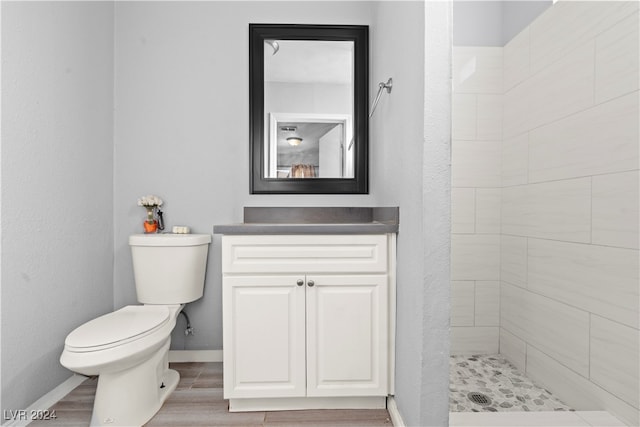 bathroom with a tile shower, hardwood / wood-style floors, vanity, and toilet