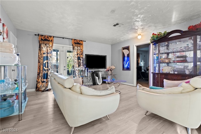 living room with a textured ceiling, light hardwood / wood-style flooring, and french doors