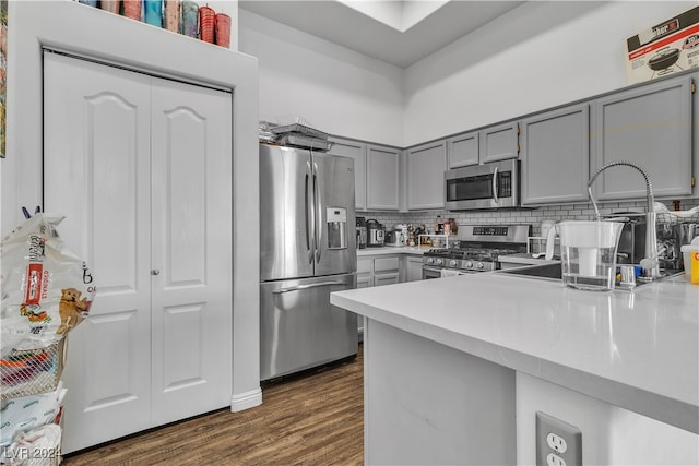 kitchen with decorative backsplash, stainless steel appliances, gray cabinetry, dark hardwood / wood-style flooring, and kitchen peninsula