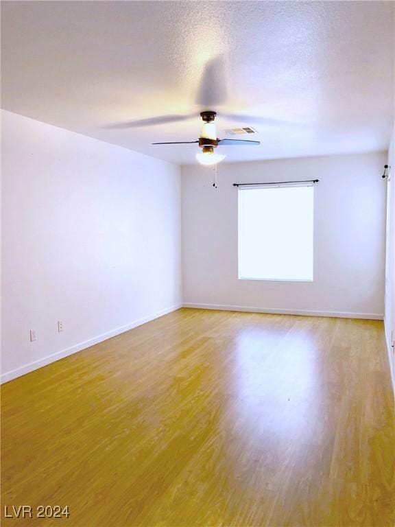 empty room featuring a textured ceiling, light wood-type flooring, and ceiling fan