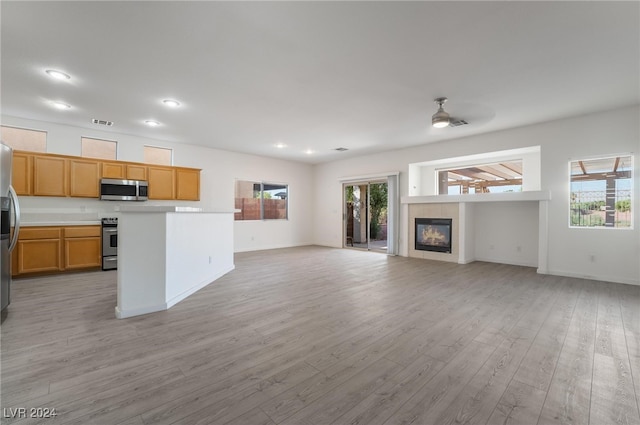 kitchen with light wood-type flooring, a tiled fireplace, a kitchen island, stainless steel appliances, and ceiling fan