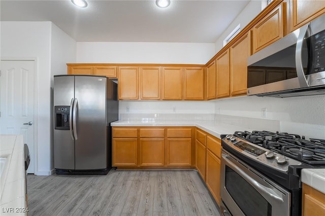 kitchen with stainless steel appliances, tile countertops, and light wood-type flooring