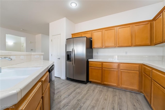 kitchen with stainless steel appliances, tile counters, light wood-type flooring, and sink