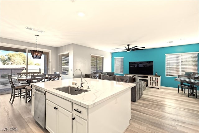 kitchen featuring hanging light fixtures, white cabinets, light wood-type flooring, a center island with sink, and sink