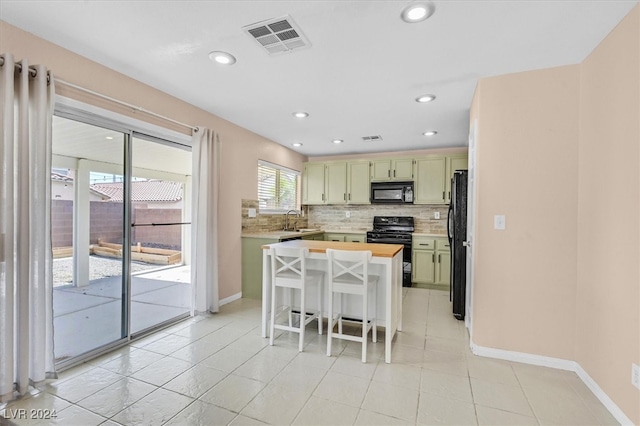 kitchen featuring decorative backsplash, a breakfast bar, black appliances, sink, and green cabinets