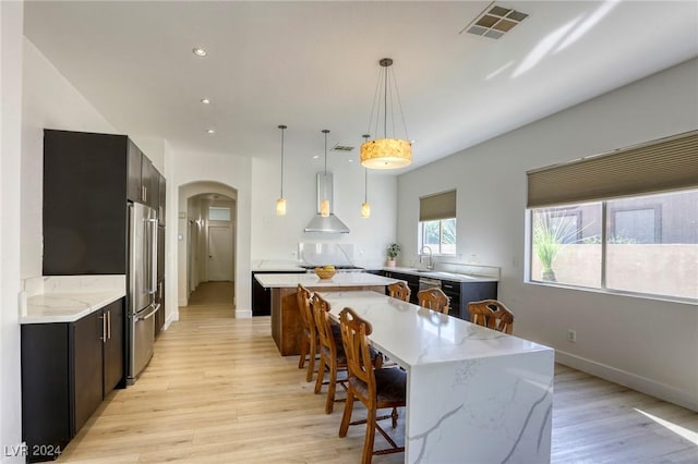 kitchen with a center island, light stone counters, pendant lighting, exhaust hood, and light wood-type flooring