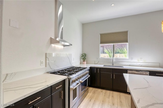 kitchen featuring light wood-type flooring, light stone counters, sink, wall chimney range hood, and double oven range