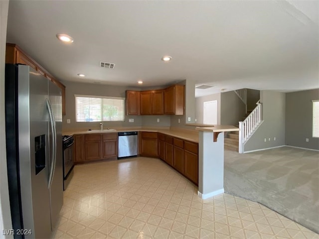 kitchen with appliances with stainless steel finishes, a breakfast bar, kitchen peninsula, sink, and light colored carpet